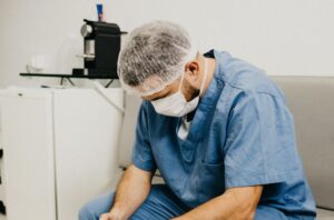 a stressed surgeon in blue scrubs looks at the floor